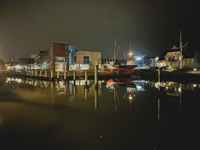 Der Husumer Hafen im Dunkeln, Gebäude und Schiffe spiegeln sich im Wasser